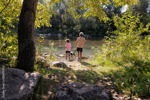 Two young boys and their dog stand by a river in a park in Summer