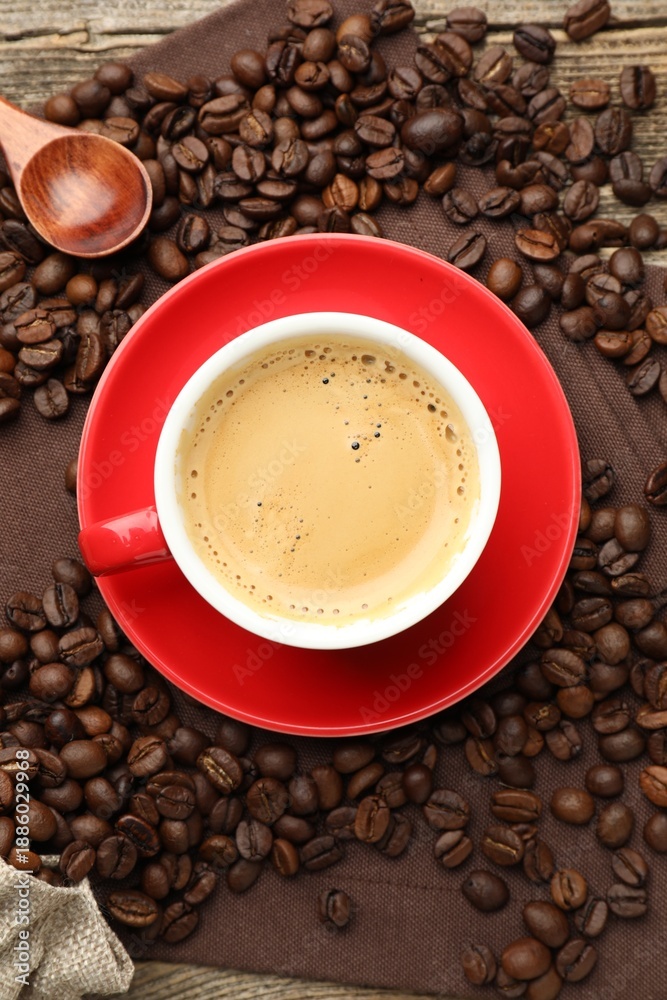 Obraz premium Cup with aromatic coffee, beans and napkin on wooden table, flat lay