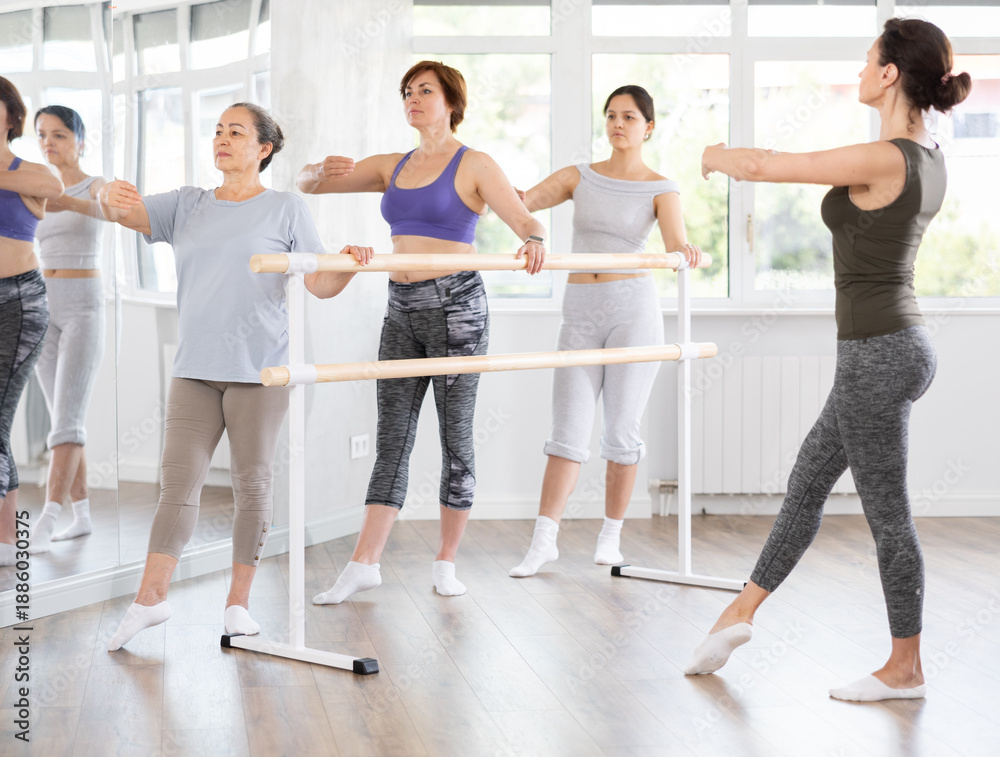 Fototapeta premium Adult female teacher showing ballet moves to group of beginner women in studio