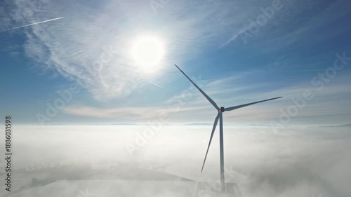 Wind turbine generating electricity in thick fog with sun shining above and clouds below