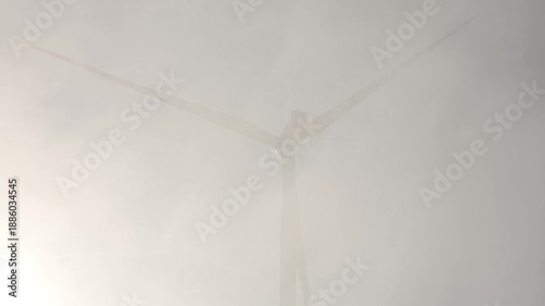 Wind turbine generating electricity in thick fog with sunlight breaking through clouds