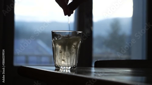 Glass of water filled with a scoop of powdered supplement which is poured in and then mixed with a teaspoon