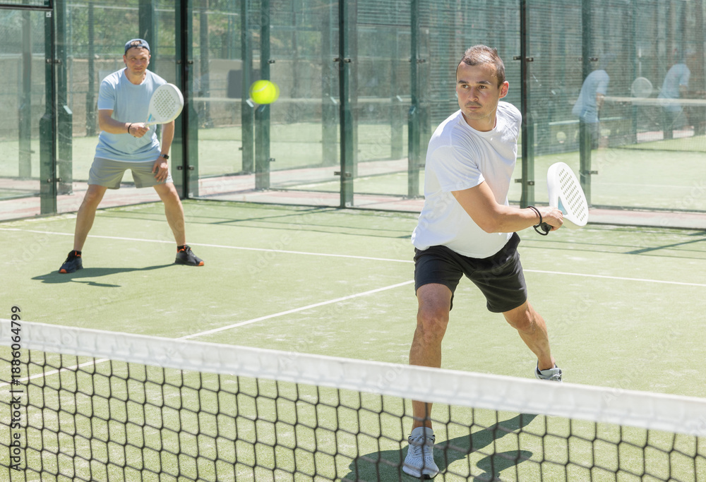 Obraz premium Men play padel on an outdoor tennis court. Hitting the ball with a racket