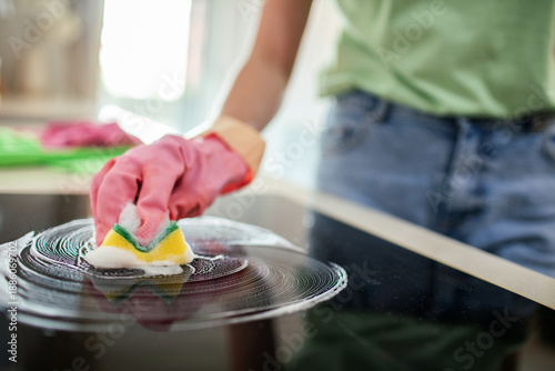 Person cleaning glass cooktop with sponge in home kitchen