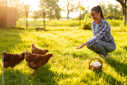 Schilderij op canvas Smiling young female farmer sitting near group of free ranging chickens walking