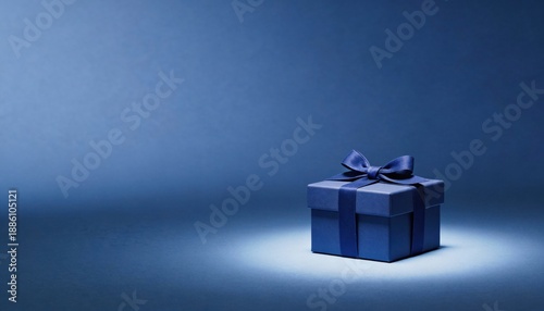 Elegant blue gift box with satin ribbon and bow, spotlighted on a dark blue background