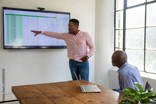 Quadro su tela African American men presenting and pointing at spreadsheet on monitor in meetin