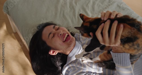 Happy Young Asian Woman Playing with Calico Cat in Sunny bedroom - Lifestyle and Pet Ownership Concept	