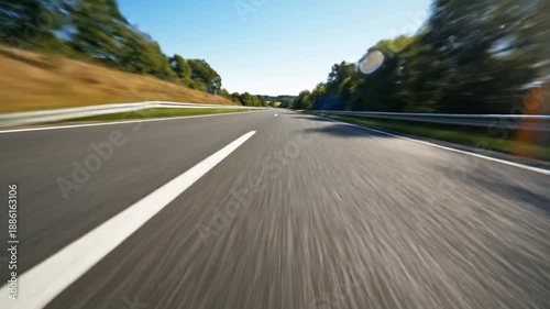 A low-angle view of a road with motion blur on the asphalt guardrails and trees beneath a clear sky