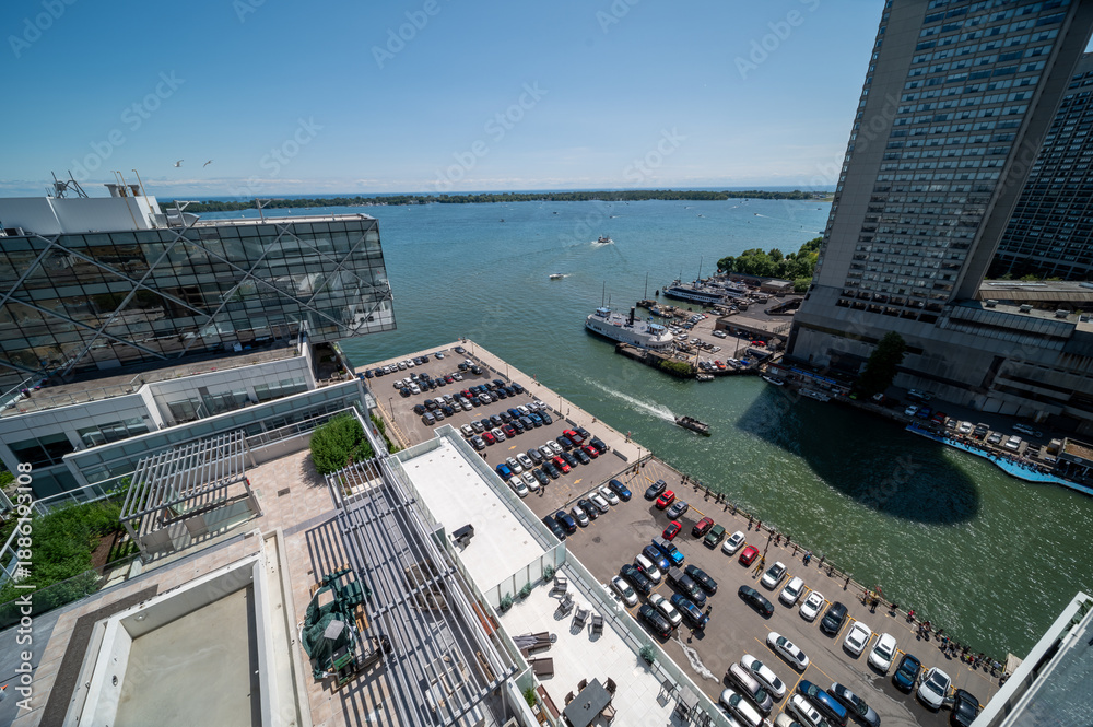 Fototapeta premium Toronto's busy waterfront features modern architecture, a parking lot, marina with various boats, and the vast expanse of lake ontario under a clear blue sky