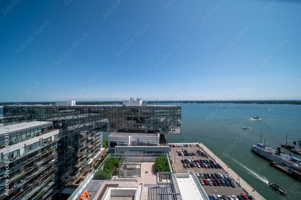 Fototapeta premium Toronto's vibrant lakefront showcasing modern residential and commercial architectures, an urban garden rooftop, bustling harbor activity, and the tranquil lake ontario under a clear summer sky
