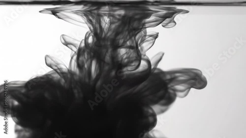 Dramatic black ink drop spreading in clear water creating unique patterns