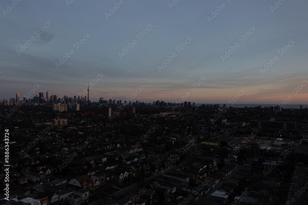 Fototapeta premium Toronto cityscape showcasing iconic skyscrapers and a vast urban core blending into a residential neighborhood at twilight, with the lake visible on the horizon