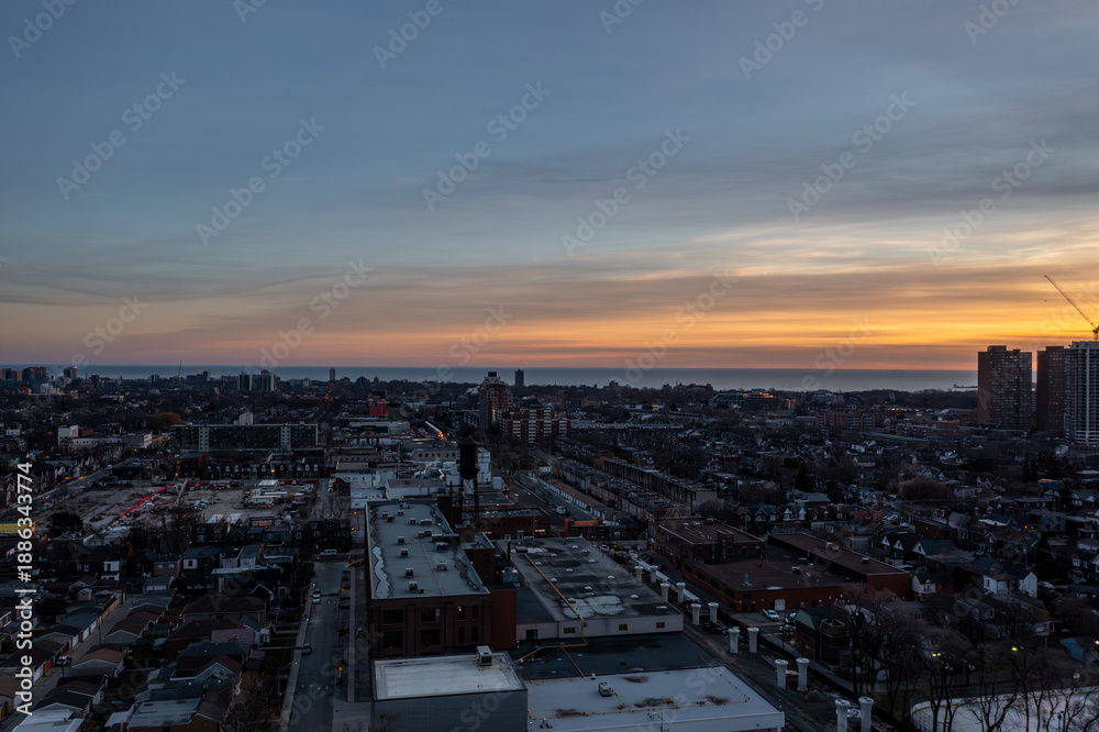 Fototapeta premium Toronto skyline with residential and industrial buildings stretching along lake ontario, bathed in warm golden hour light as dusk paints the sky orange and blue over the cityscape