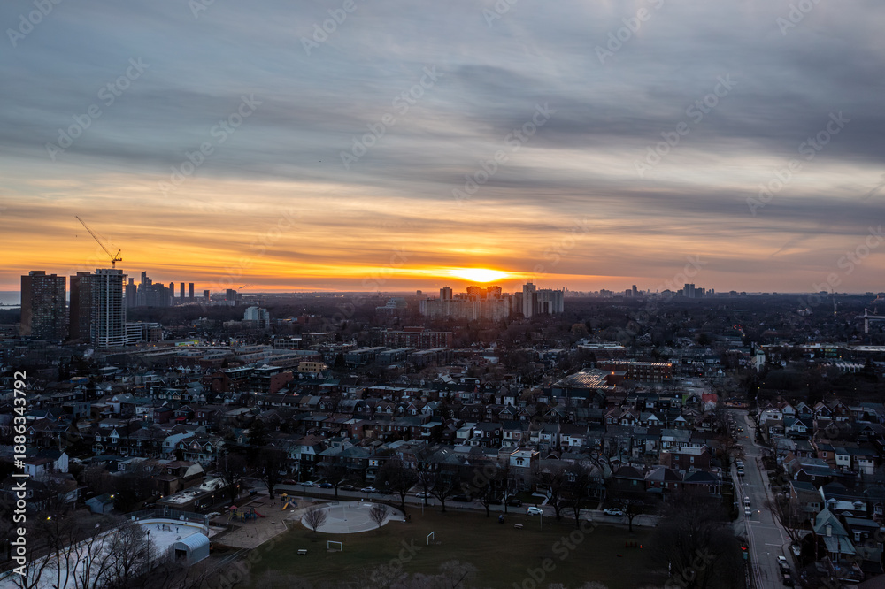 Fototapeta premium Toronto city landscape with residential homes and apartment buildings glowing under a vibrant sunset sky, highlighting the urban environment and tranquil evening light