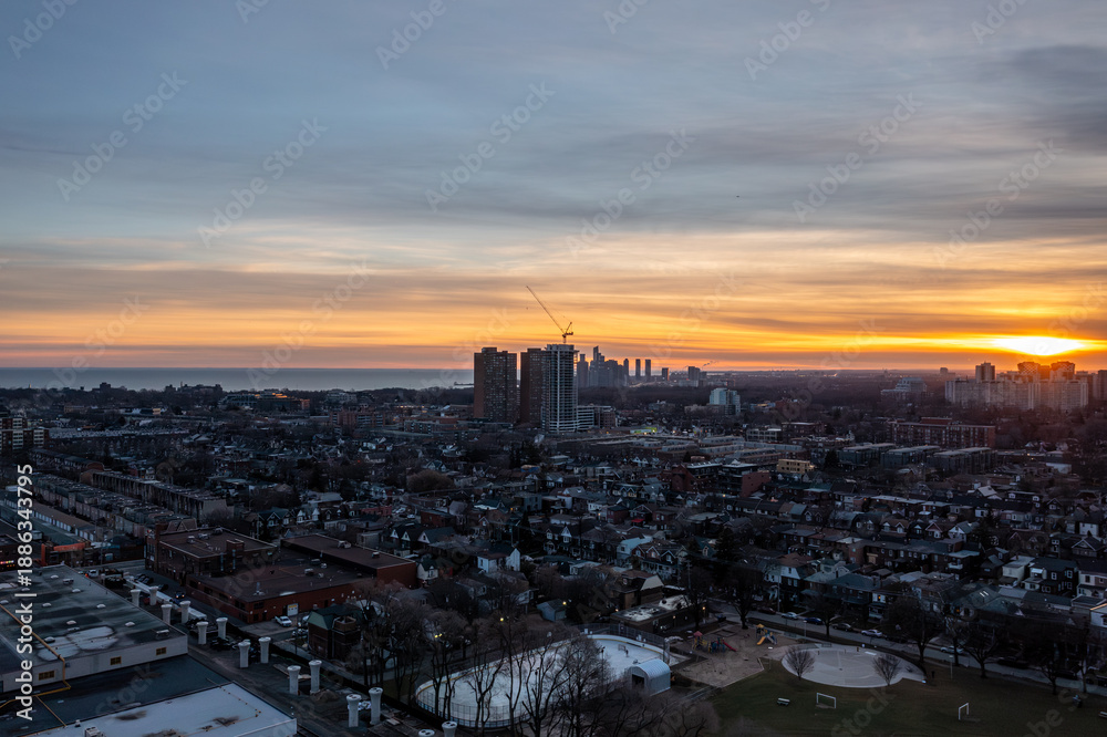 Fototapeta premium Toronto skyline at dusk with residential streets, high rises, a construction crane and lakeside park with an ice rink, golden hour view toward lake ontario and the horizon