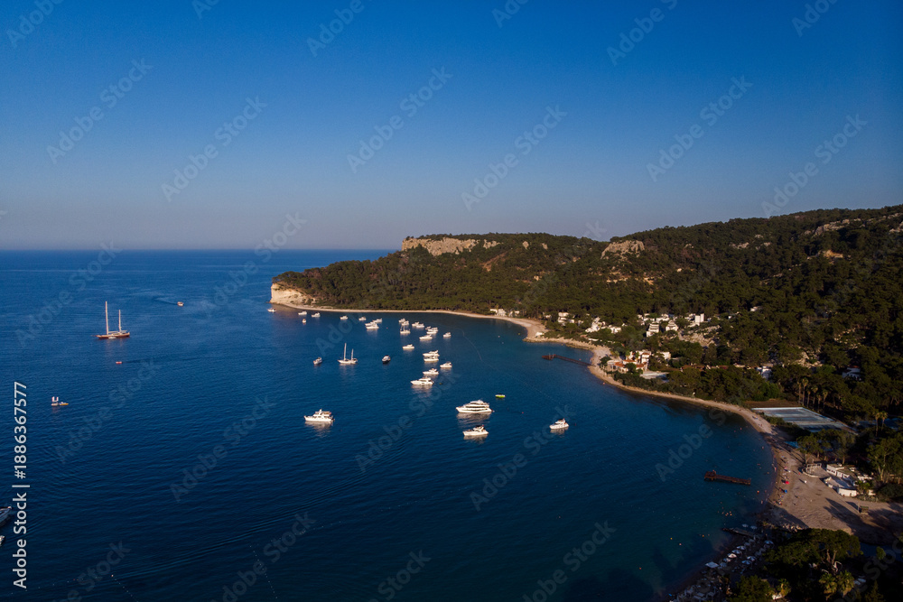 Fototapeta premium Luxury yachts moored in quiet bay. Aerial view of a tranquil marina with a tropical coastal area, surrounded by lush green forest and crystal clear turquoise water. Turkey Resorts