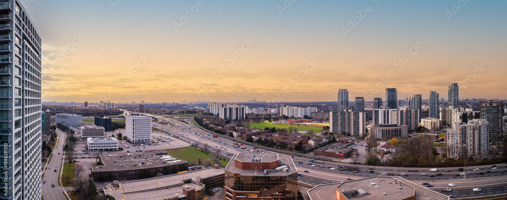 Fototapeta premium Mississauga city panorama showcasing modern skyscrapers, residential buildings, and the busy highway with car traffic flowing during a golden hour twilight