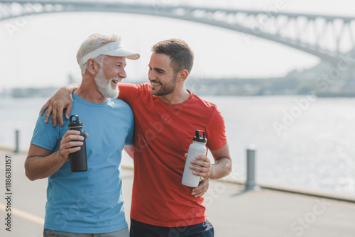 Father and son smiling and holding water bottles after exercising outdoors 
