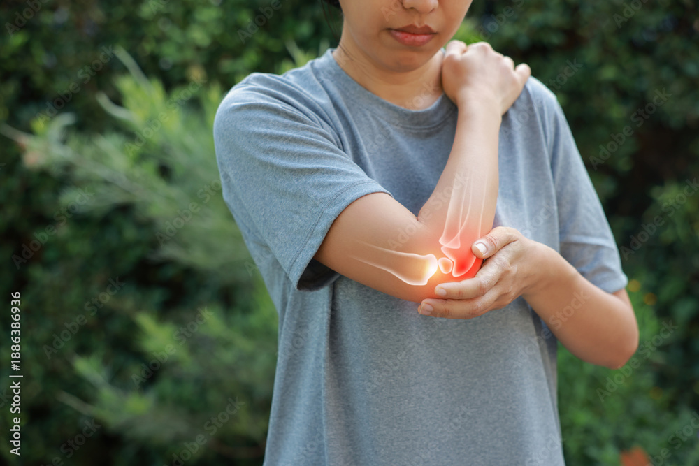 Fototapeta premium Close-up woman holding painful injured elbow with red inflamed spot and X-ray bone skeleton overlay. Medical concept of joint pain, fracture, arthritis, tendonitis, muscle injury, outdoor background.