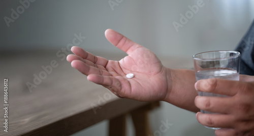 man hand holds a white pill or capsule and a glass of water at home, eating vitamin on time, medicine daily vitamins ginseng or calcium support health, wellness, health and care. © onephoto