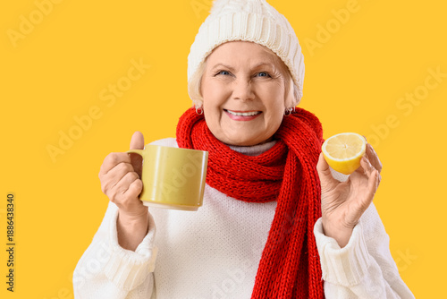 Sick elderly woman with cup of tea and lemon on yellow background