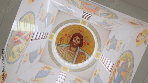 Low angle view of modern religious murals and icons on church walls. Beautiful contemporary Byzantine art with golden details and sunlight in a sacred space