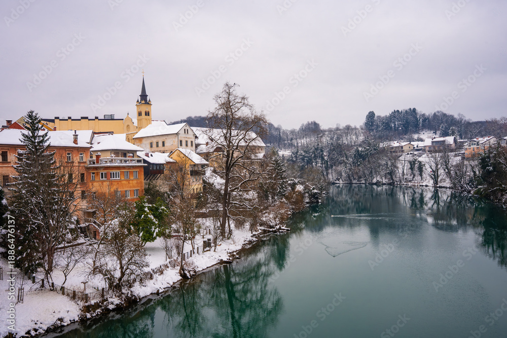 Obraz premium The picturesque town of Novo Mesto in Slovenia during winter, covered in snow, showing beautiful facades and houses along the colorful Krka River. Novo Mesto, Slovenia 09.01.2026 