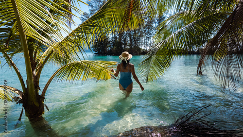Bilde på lerret A traveler enjoys the tranquil vibes of Khlong Hin Beach in Koh Kood, Thailand, wading through sparkling turquoise waters surrounded by lush palm trees