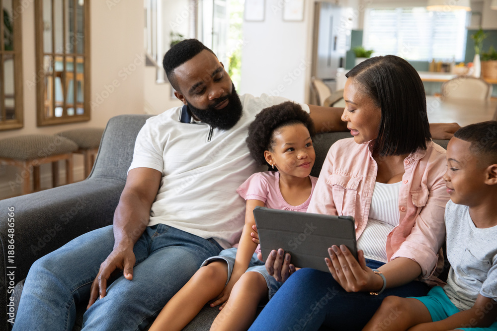 Fototapeta premium African American family sitting together and interacting with tablet on gray couch in living room