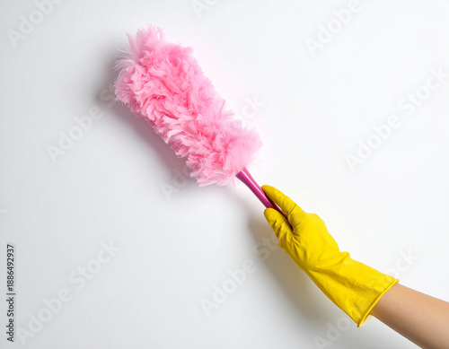 Yellow gloved hand holding a fluffy pink duster with a pink plastic handle against a white wall