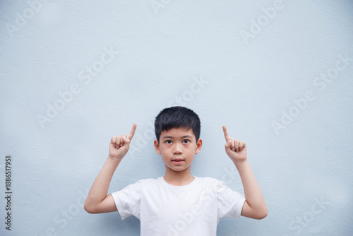An Asian boy wearing a white shirt is pointing to the side in a blank space for text, against a gray background.