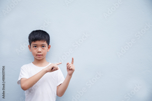 An Asian boy wearing a white shirt is pointing to the side in a blank space for text, against a gray background.