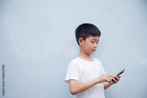 An Asian boy is playing a game on his smartphone with a workspace in the background.