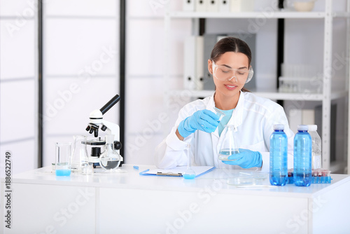 Happy female young scientist with professional glassware and clipboard examin...