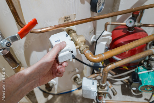 Slika na platnu Central heating plumber seen adjusting a water flow control valve for hot water that feeds to a consumer hot water tank