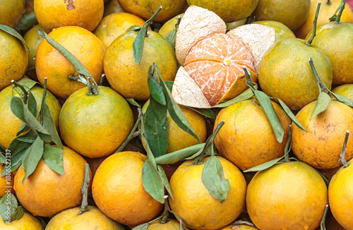 Fresh organic tangerines with green leaves and one peeled fruit showing juicy segments at market.