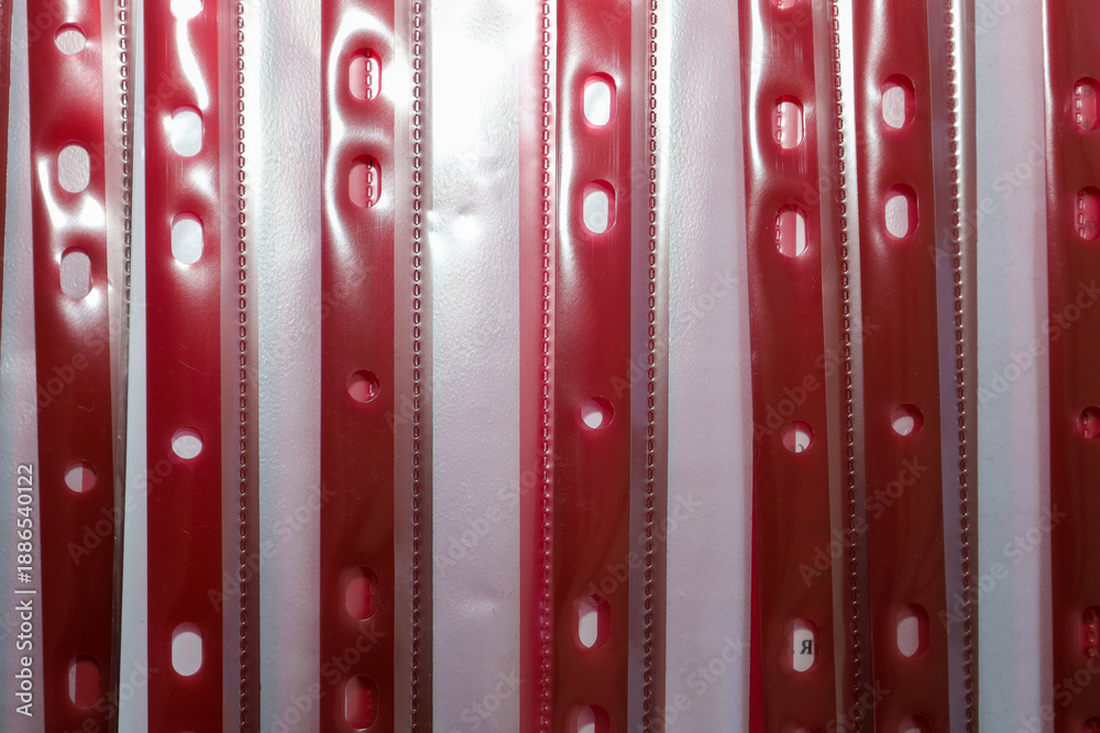 Obraz premium Vertical stripes of red plastic file pockets with perforation for document archiving arranged in a row. Abstract background of stationery supplies for organizing paper workflow in the office or at hom