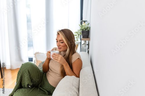 Bilde på lerret Portrait of a happy young woman sitting by a window, drinking coffee and looking thoughtfully outside