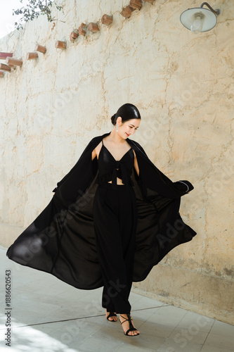 A full-length woman in a black abaya against a street background in soft natural light. Traditional Arab-Muslim clothing.