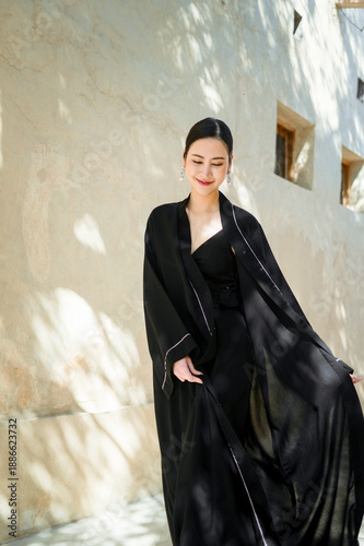 A full-length woman in a black abaya against a street background in soft natural light.