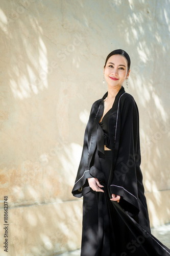 A full-length smiling woman dressed in a black abaya is captured in natural light. Traditional Arab-Muslim clothing.