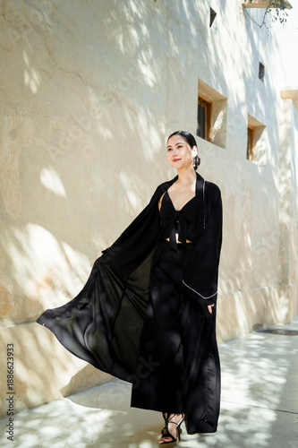 A full-length woman in a black abaya against a street background in soft natural light.