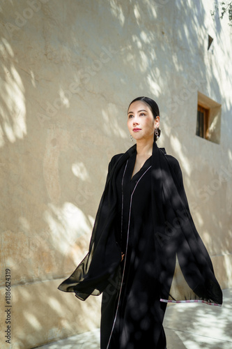 A full-length woman in a black abaya against a street background in soft natural light.