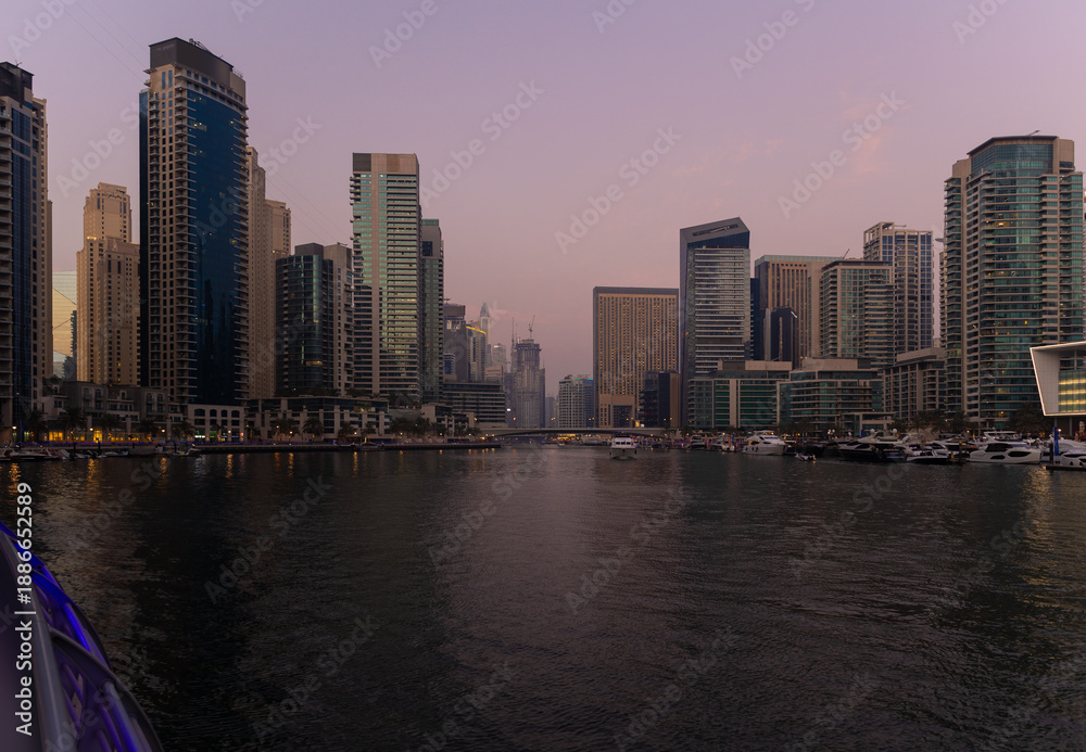 Obraz premium Evening view of the city. Orange sunlight, skyscrapers, buildings, and city streets. On the streets of the Emirates, in a public space.