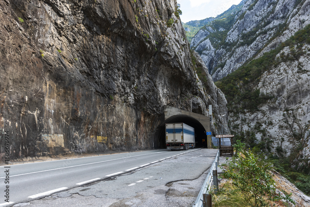 Fototapeta premium A large truck nears a dark tunnel, mountain road view