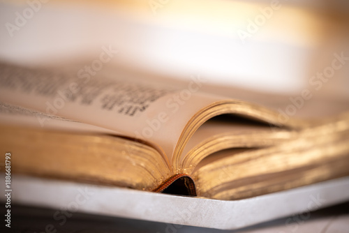 Open Bible on the altar of a church with selective focus on the gold edging of the paper pages. Atmospheric still life of the Book of Books of Christianity in the golden evening light of the sun.