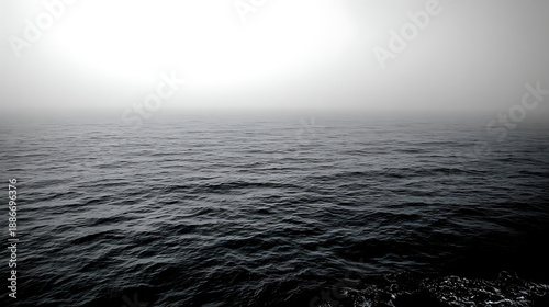 Dark ocean waves stretch toward a dense white fog on a mysterious and silent horizon, captured in a minimalist, high-contrast monochromatic style.