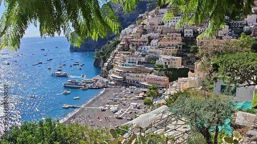 Amalfi Coast, Italy. Scenic coastal view of Positano, Italy, showcasing vibrant buildings on cliffs, sandy beach, and boats anchored in the turquoise waters under bright sunlight