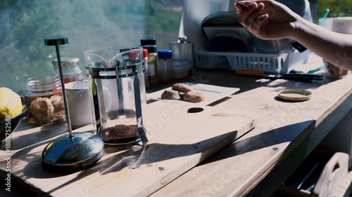 An outdoor scene with a coffee press, cookies and kitchenware on a rustic wooden table. A person's hand reaches for cookies Cederberg, South Africa